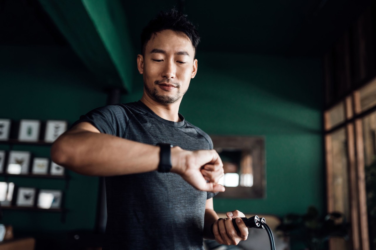 Active young Asian man exercising at home, using fitness tracker app on smartwatch to monitor training progress and measuring pulse. Keeping fit and staying healthy. Health, fitness and technology concept