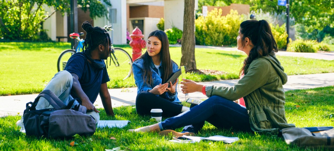 A diverse group of college students, spending time together outdoors on a college campus in the fall.